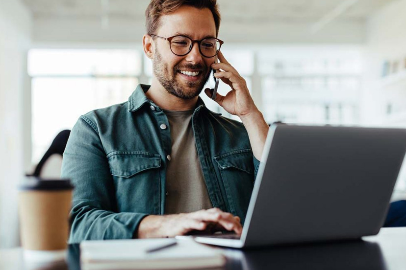 Business owner on phone call managing operations while reviewing sales data on laptop – scaling from 5 to 50 monthly deals